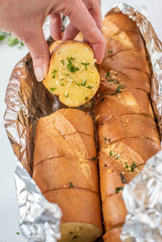 French baguette garlic bread wrapped in foil with one slice being lifted out.
