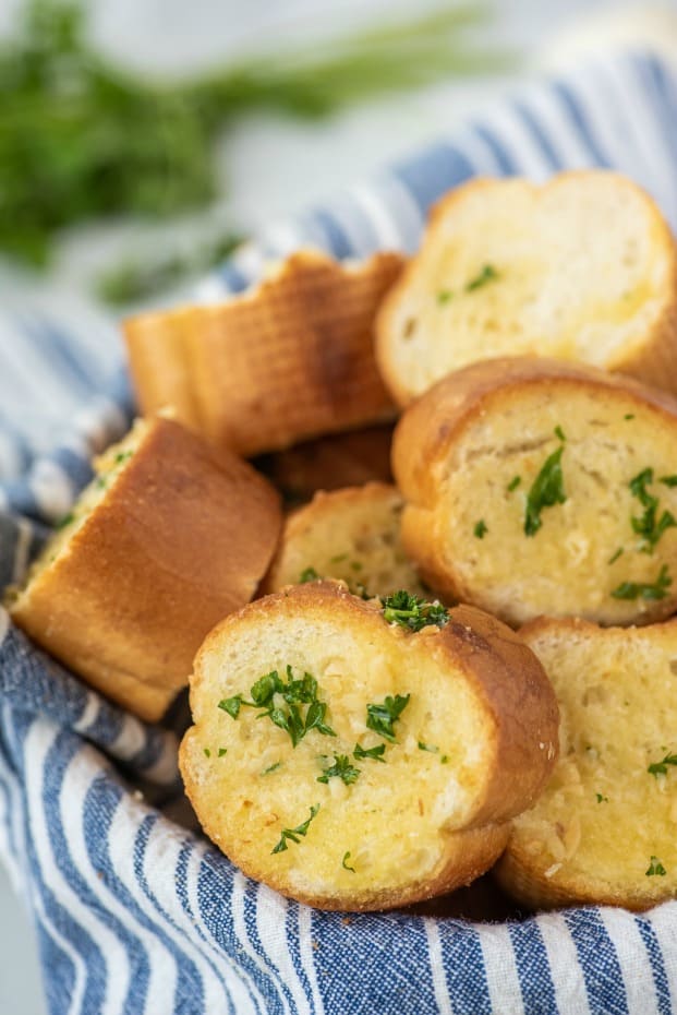 Bread bowl with blue and white striped towel filled with homemade garlic bread slices.