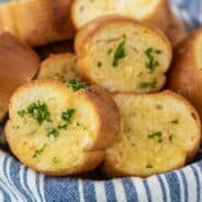 Garlic bread slices in a bowl lined with a blue striped linen towel.