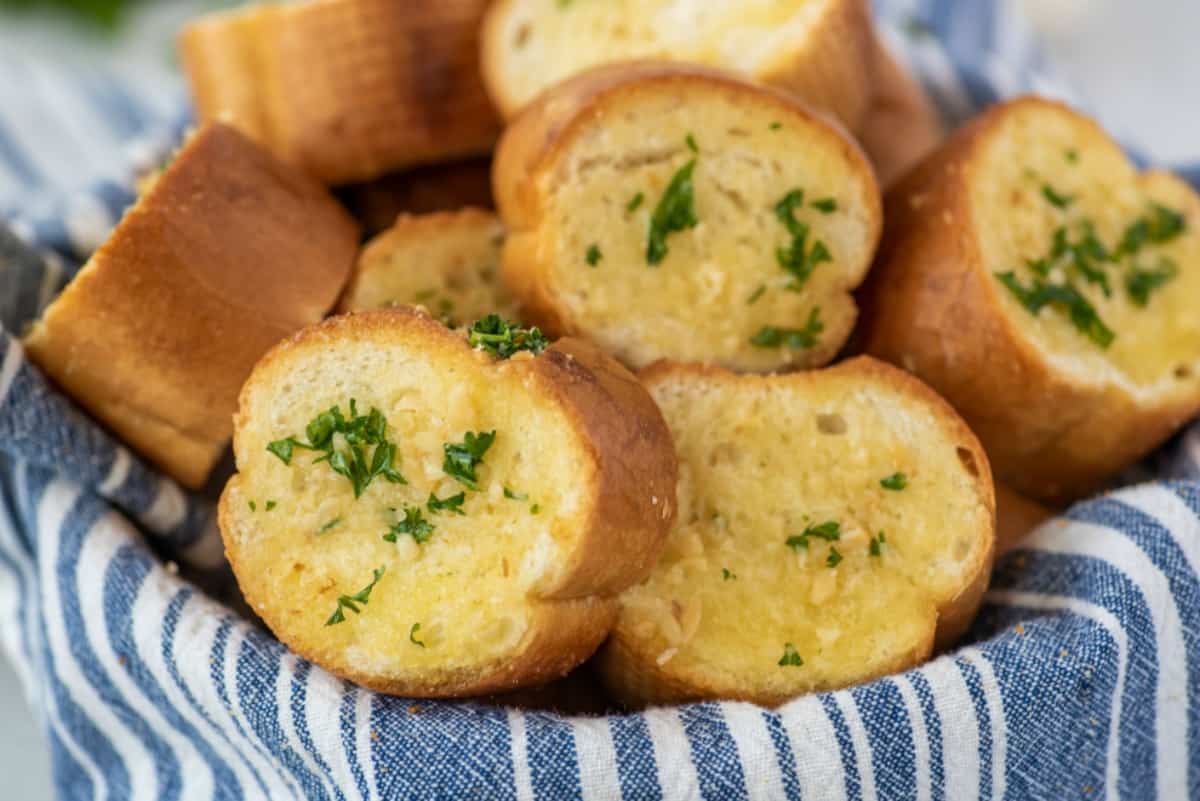 Garlic bread slices in a bowl with a blue and white striped linen napkin.