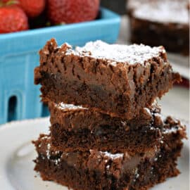 Stack of three gooey chocolate brownie bars sprinkled with powdered sugar on a white plate with red napkin.