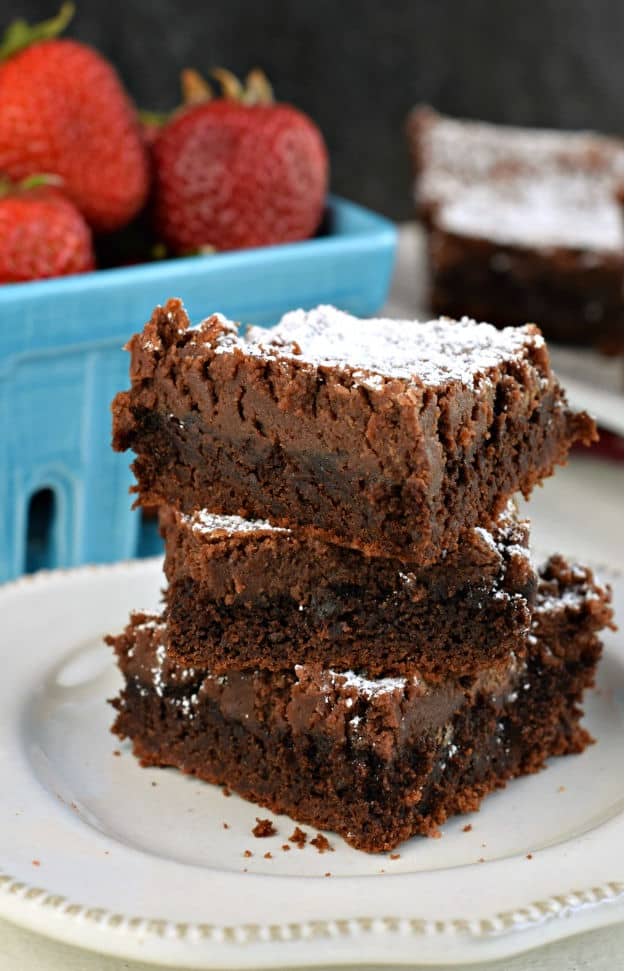 Stack of three gooey chocolate brownie bars sprinkled with powdered sugar on a white plate with red napkin.