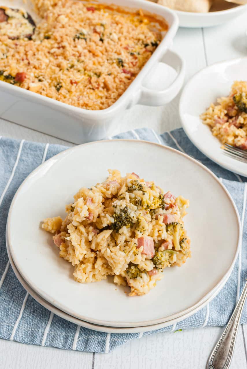 Plate of ham and rice casserole with cheese and broccoli on a blue linen napkin.