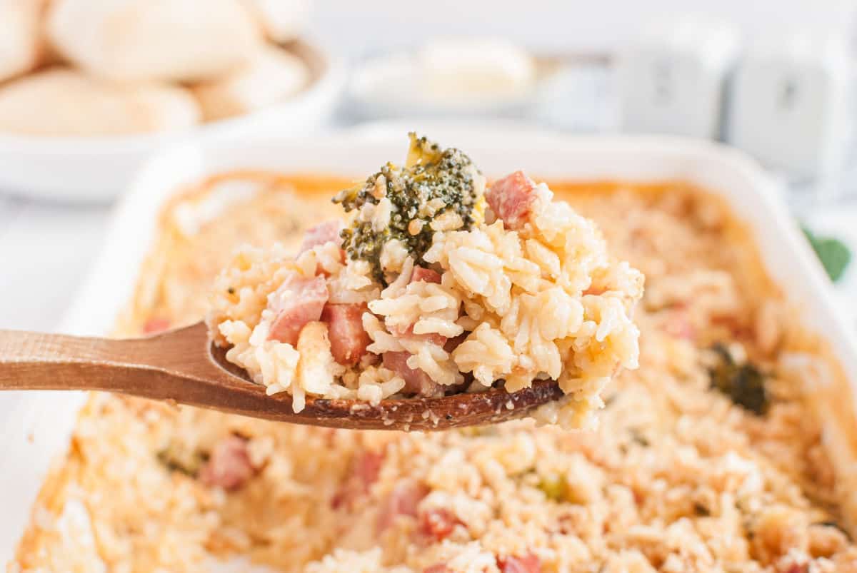 Wooden spoonful of ham casserole being scooped out of 13x9 baking dish.