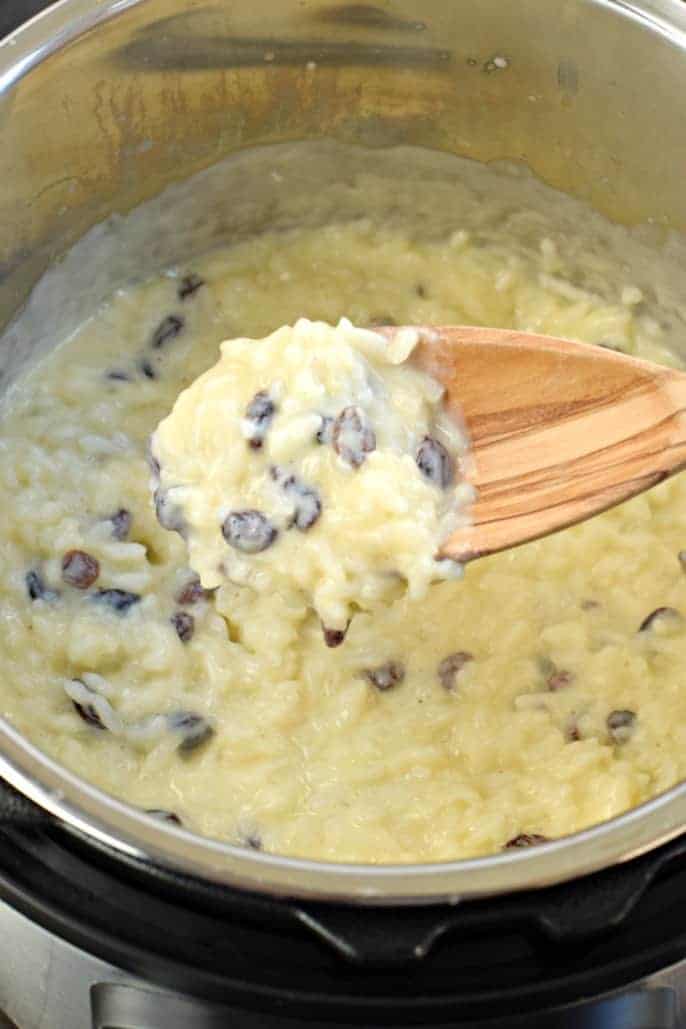 Instant Pot con un cucchiaio di legno pieno di budino di riso denso e cremoso.