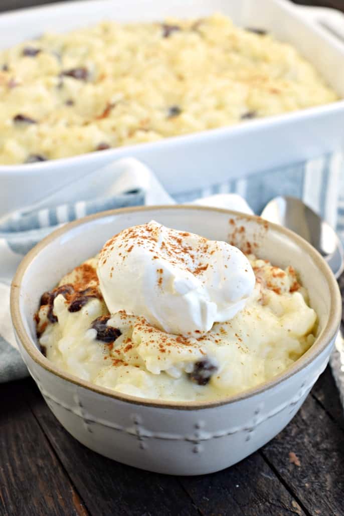 Bol blanc avec riz au lait et crème fouettée. Grand plat rectangulaire blanc rempli de riz au lait en arrière-plan.