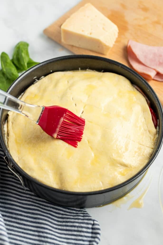 Italian torte in a springform pan being glazed with egg yolks.