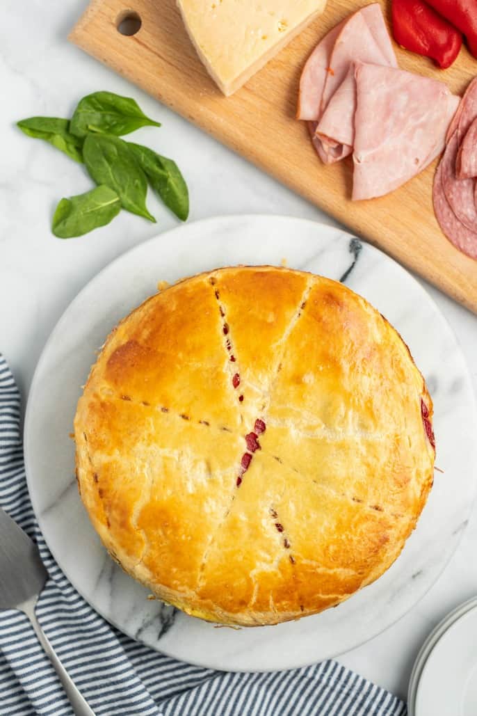 Baked Italian Sandwich torte on a marble cake plate, remove from pan, and uncut.