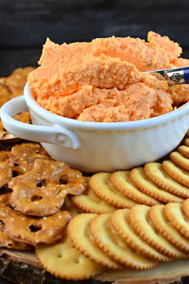 White bowl filled with pimento cheese dip on a board with crackers.