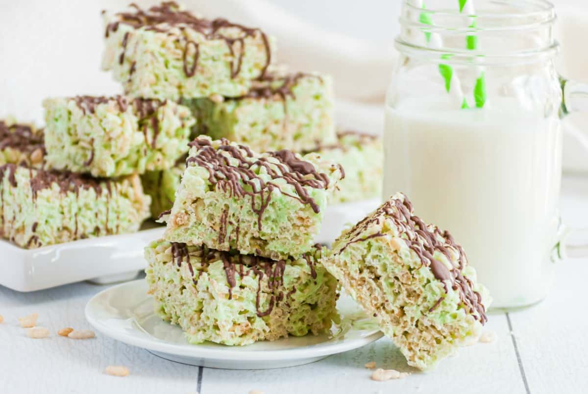 Pistachio Krispie Treats on a white plate, piled up and drizzled with dark chocolate.