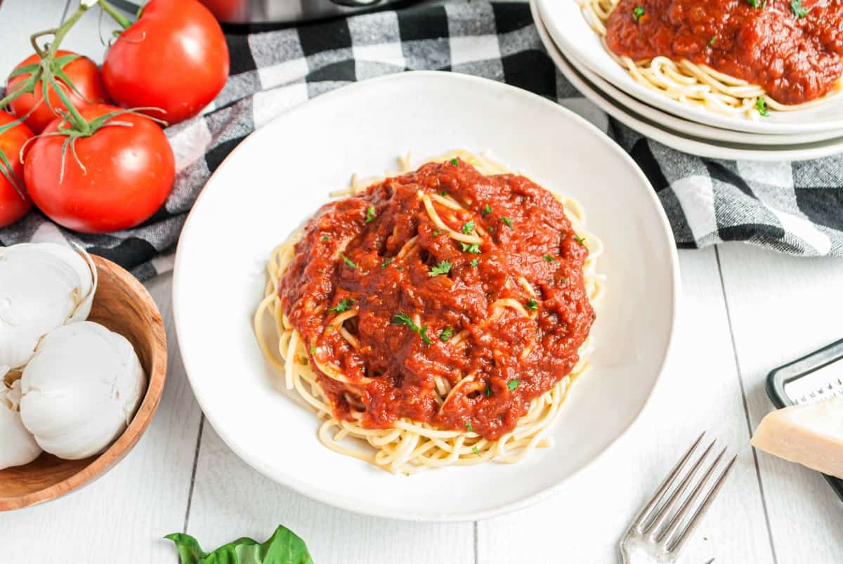 White pasta bowl with spaghetti and homemade marinara sauce. Served with a black and white napkin and fresh tomatoes on the side.