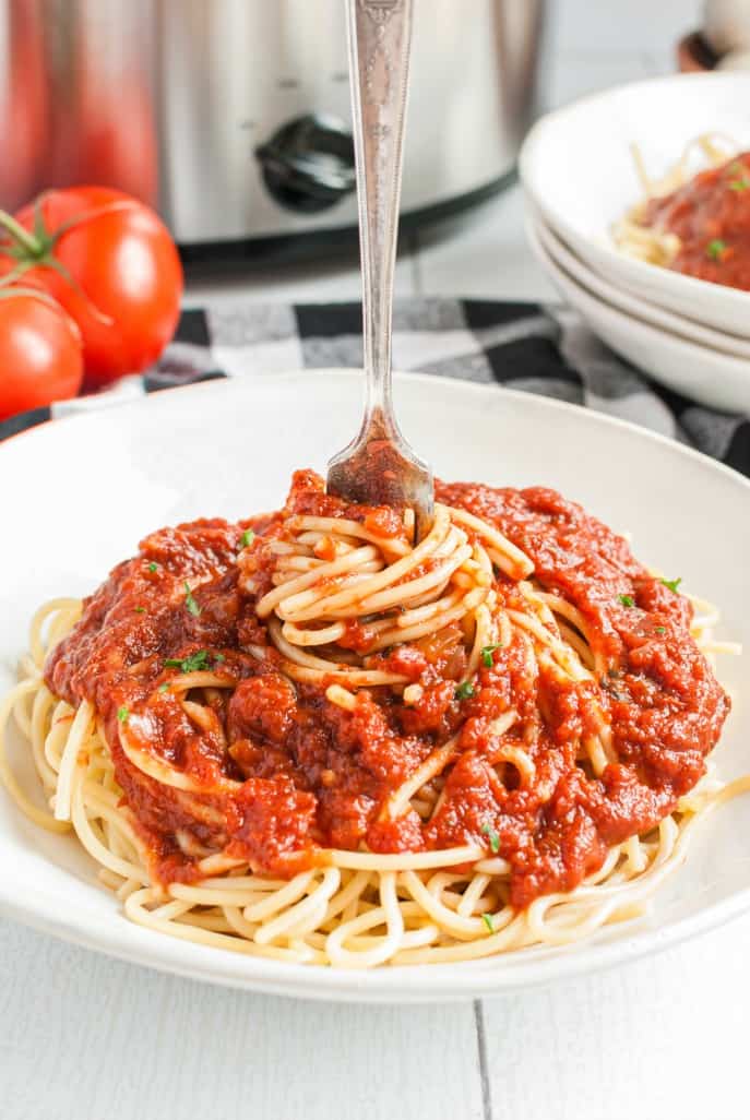 Spaghetti and sauce in a white pasta bowl with a fork twirling noodles.