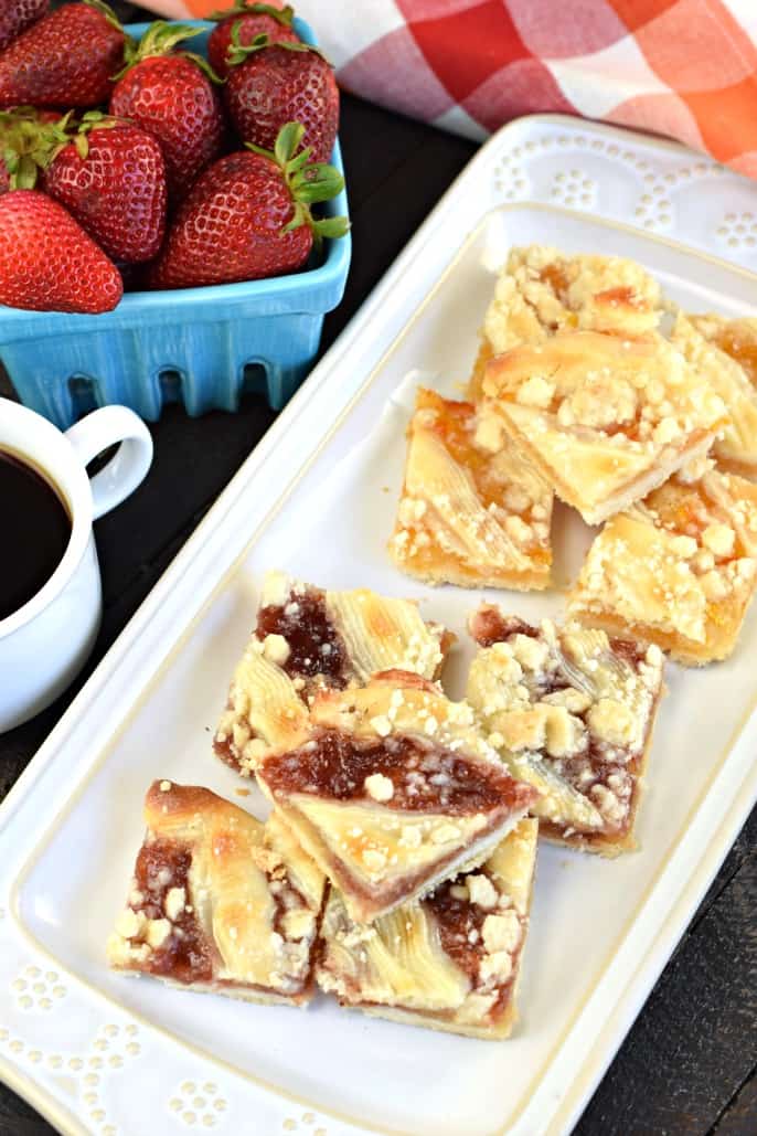 Strawberry streusel bars and orange marmalade bars topped with cream cheese on a white plate.