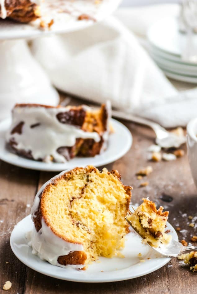 Silver fork with a bite full of cinnamon bundt coffee cake and vanilla glaze on a white plate.