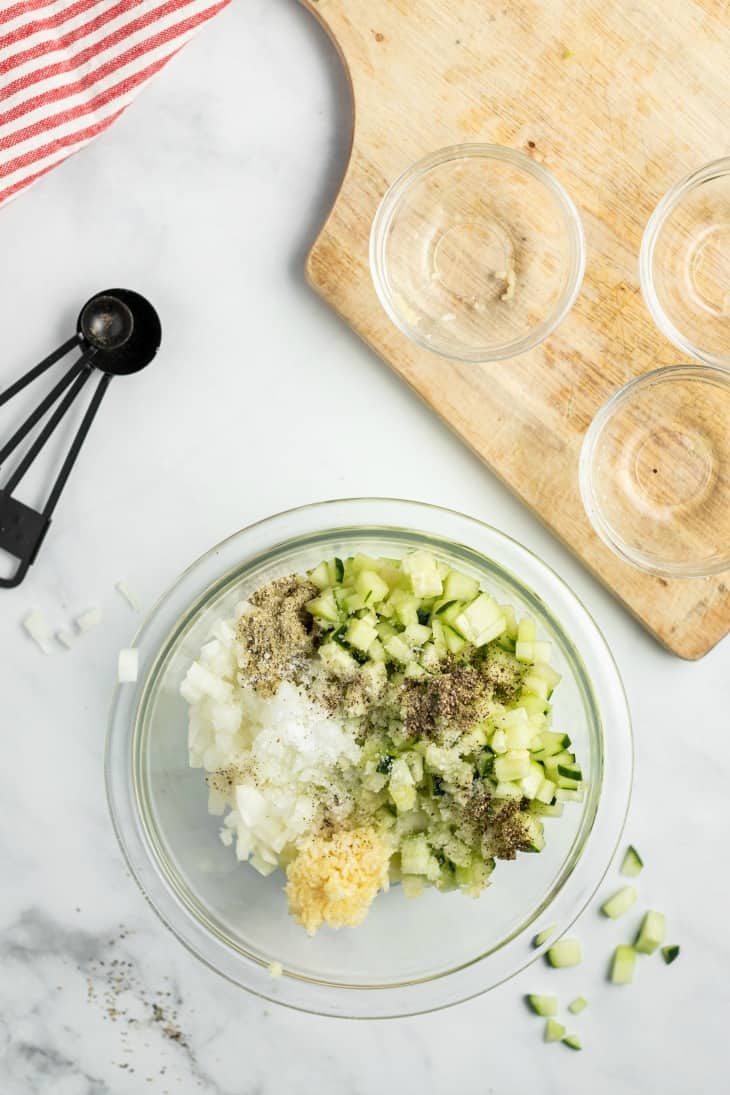 All the ingredients for greek tzatziki sauce in a clear glass bowl before being mixed together.