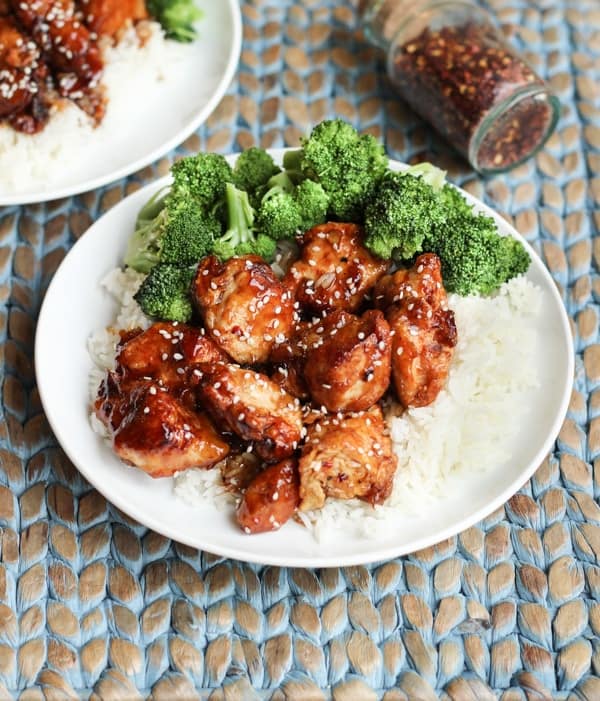 White plate with rice, chicken, and broccoli topped with sesame seeds.