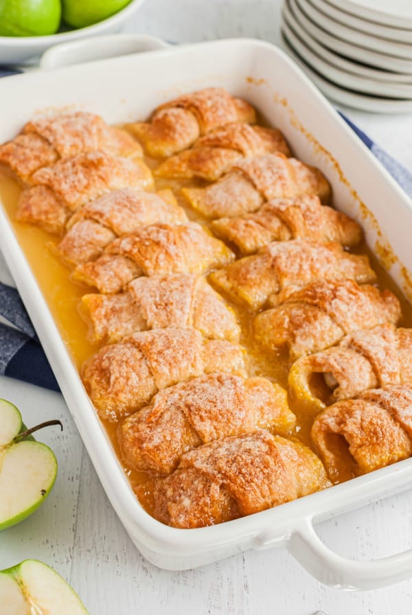 White 13x9 baking dish with apple dumplings in sugar syrup sauce.
