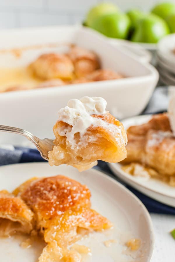 Plate of apple dumplings with one forkful being lifted up and topped with melted vanilla ice cream.