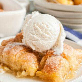 White dessert plate with several apple dumplings and a big scoop of vanilla ice cream on top.