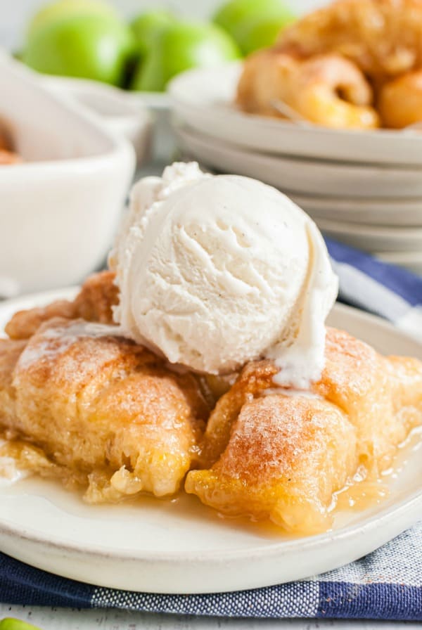 White dessert plate with several apple dumplings and a big scoop of vanilla ice cream on top.