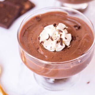 Clear glass dessert dish with chocolate pudding. Topped with whipped cream, chocolate shavings, and a gold spoon on the side.