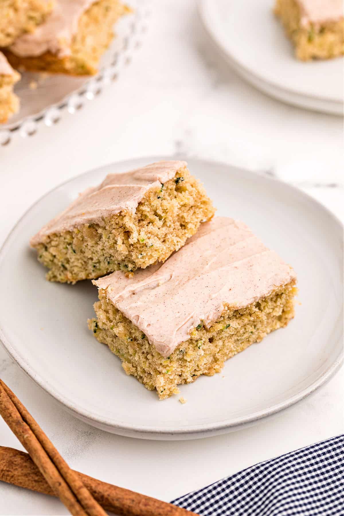 Two zucchini bars with cinnamon frosting served on a white dessert plate.