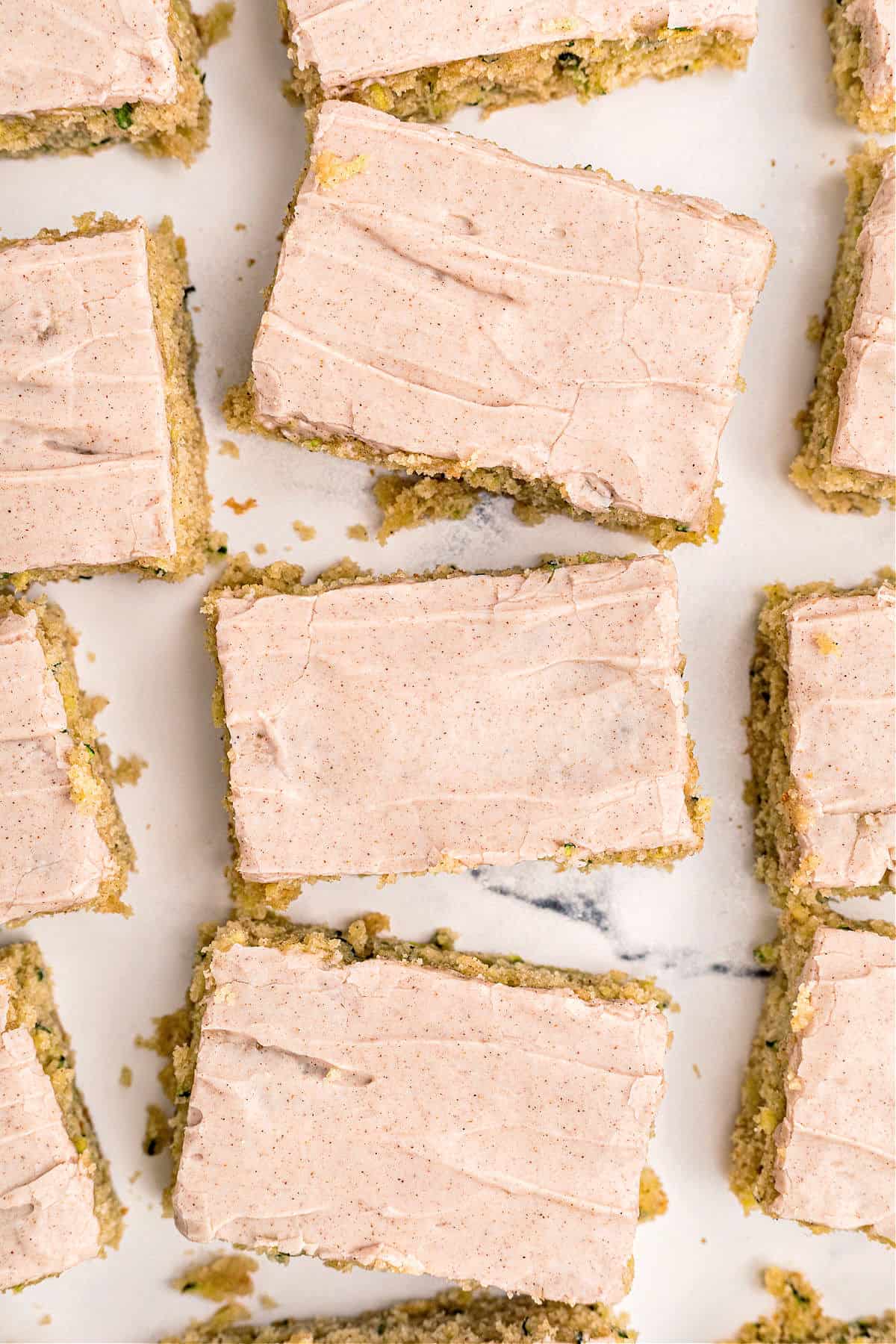 Cinnamon frosted zucchini bars cut into squares on white parchment paper.