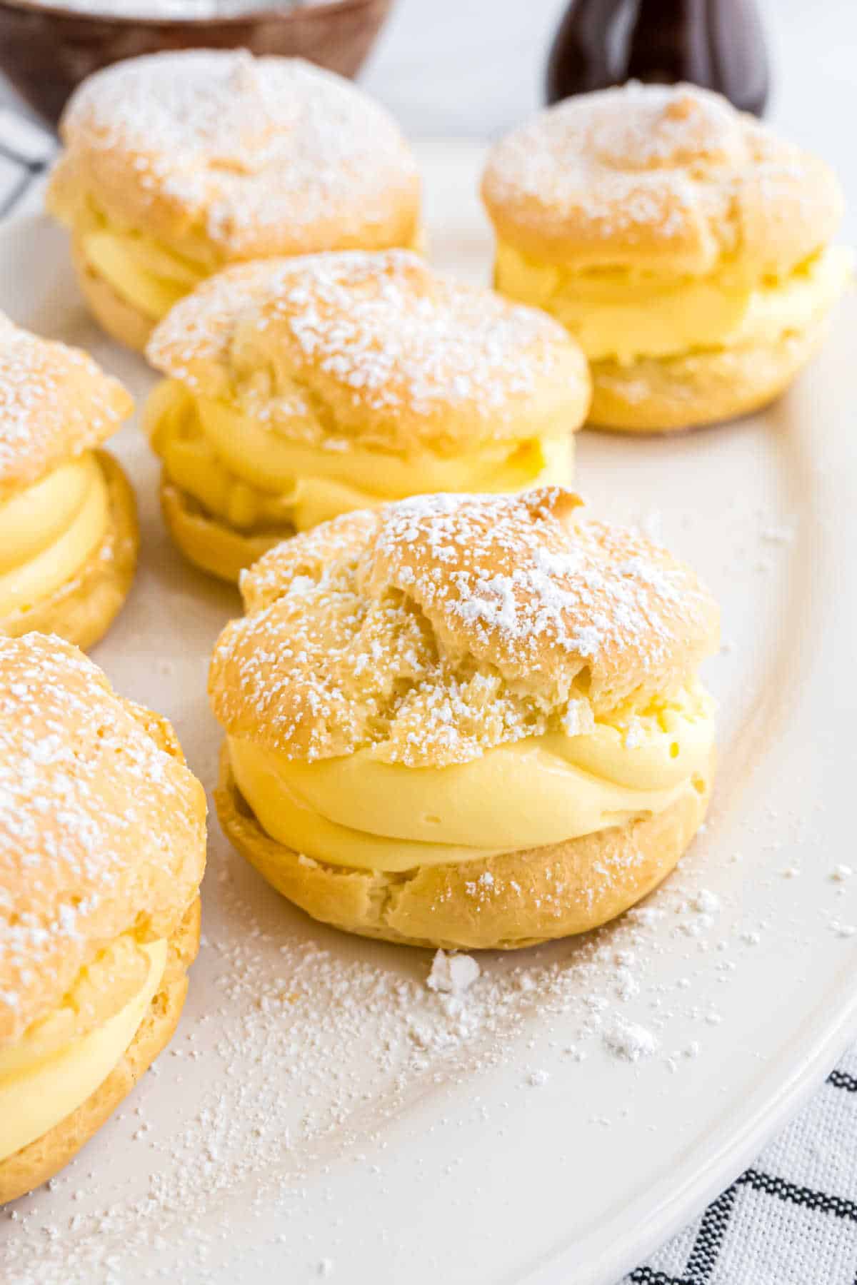 Cream puffs filled with yellow custard and topped with powdered sugar on a white plate make for an irresistible cream puff dessert.