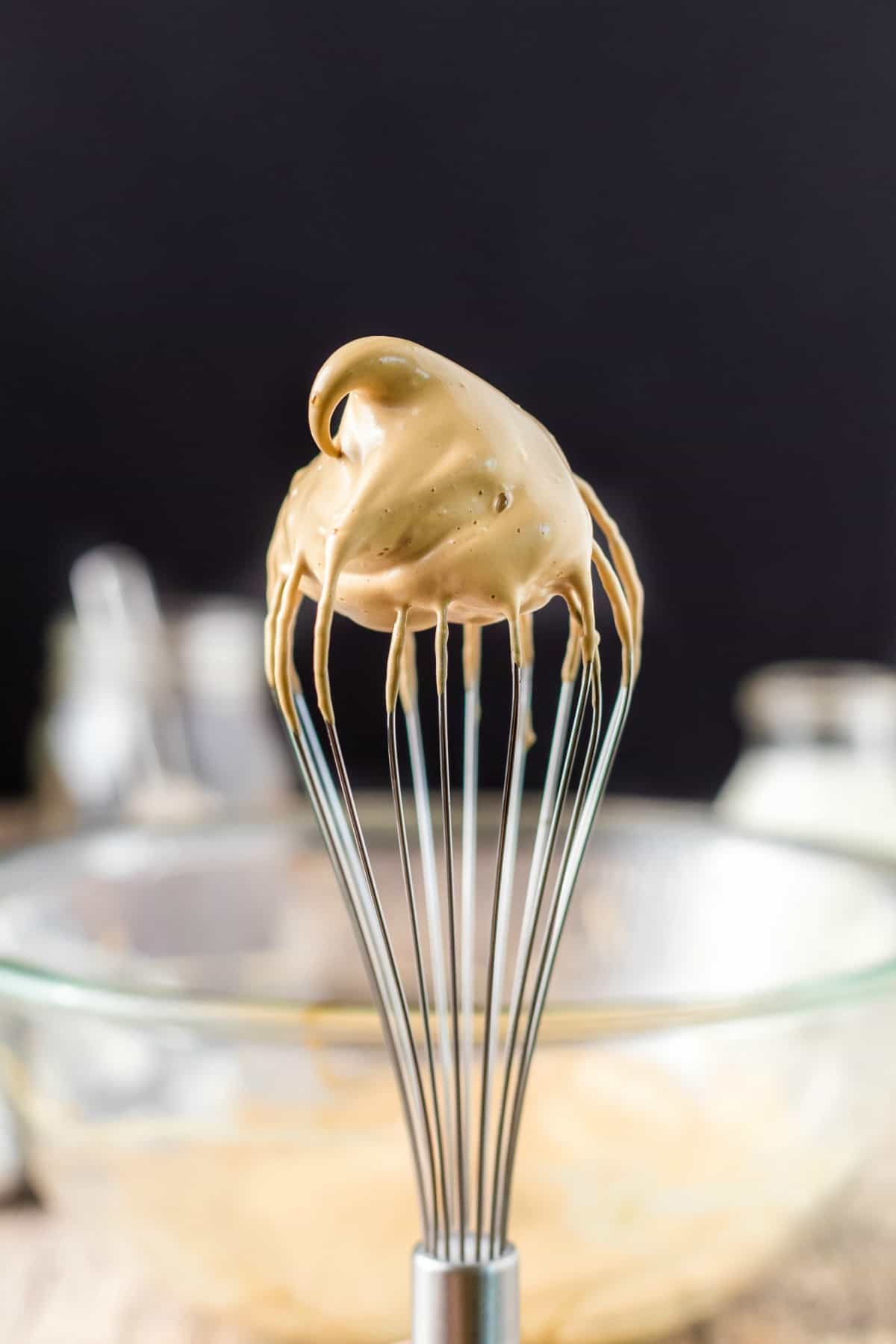 Whisk held upright with big swirl of whipped coffee in a stiff peak.