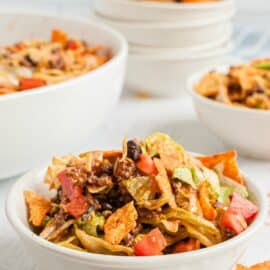 Taco salad in white dinner bowls topped with doritos.