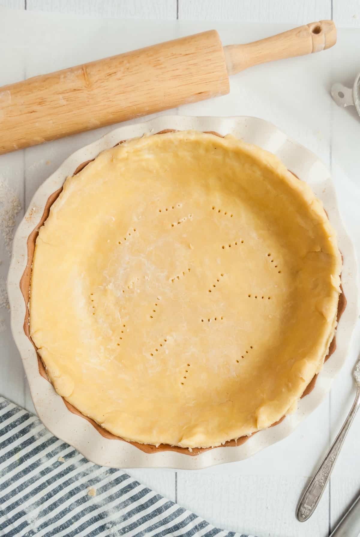 Homemade pie crust in a pie plate before baking with a rolling pin in background.