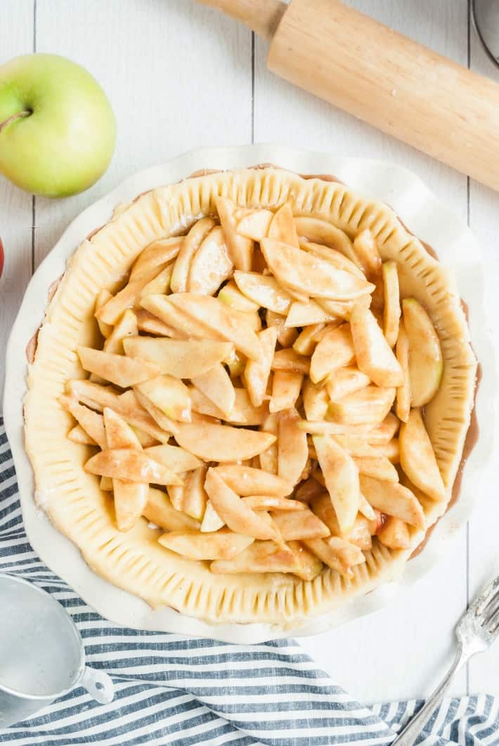 Pie crust in a pie plate filled with apple slices before baking.