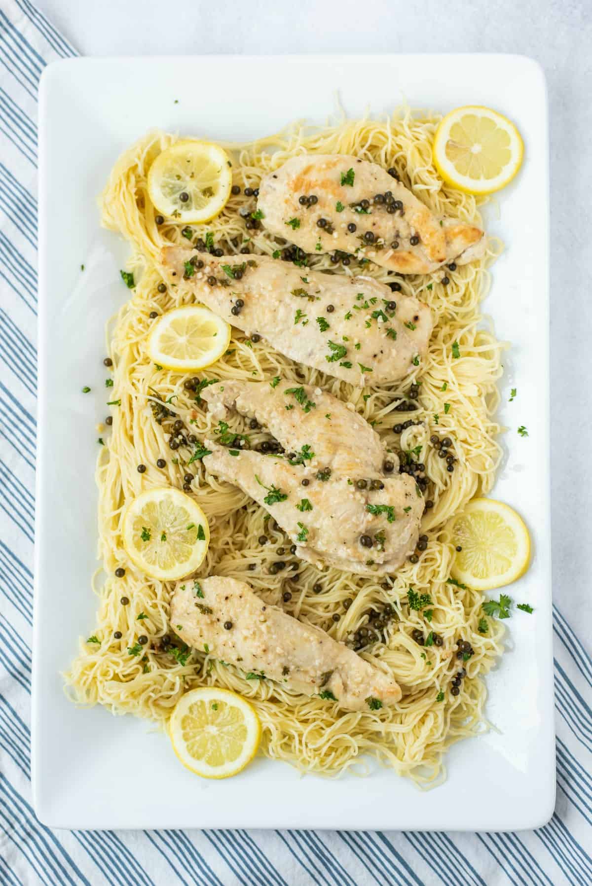 White rectangular serving plate topped with angel hair pasta and chicken piccata.