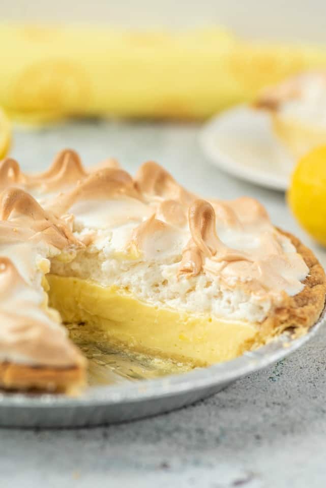 Lemon meringue pie in a metal pie plate with one slice removed.