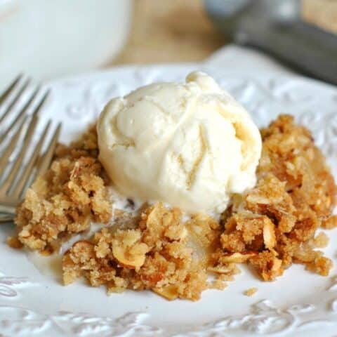Peach crisp spooned onto a white plate with a scoop of vanilla ice cream.