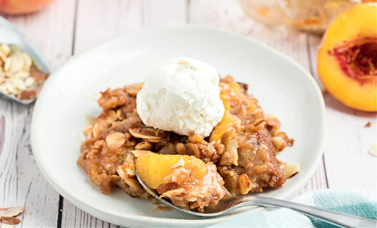 White plate with peach crisp and scoop of vanilla ice cream.