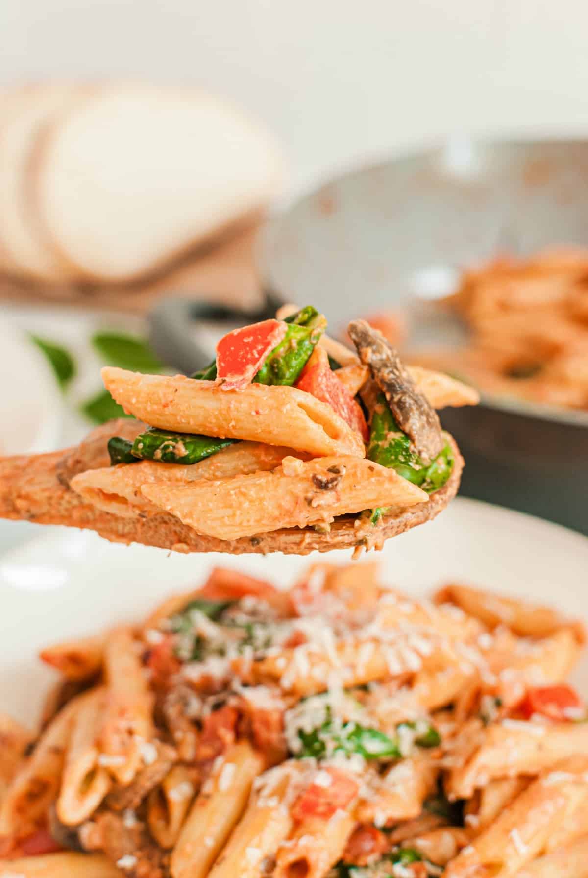 Wooden spoon with a scoop of penne pasta lifting out of the skillet.