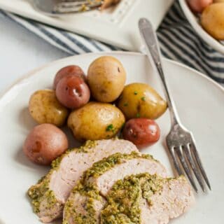 White dinner plate with slices of pesto topped pork and small steamed potatoes.