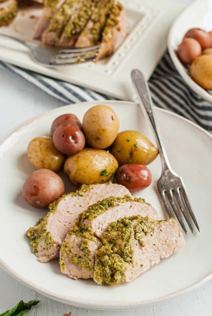 White dinner plate with slices of pesto topped pork and small steamed potatoes.