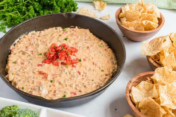 Rotel dip in a cast iron skillet with three bowls of tortilla chips on the side.