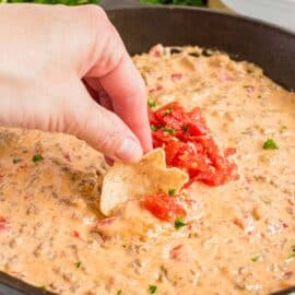 Cheesy rotel dip in a black cast iron skillet with a hand scooping dip on a tortilla chip.