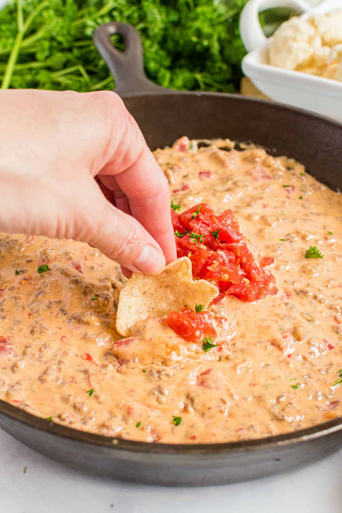 Cheesy rotel dip in a black cast iron skillet with a hand scooping dip on a tortilla chip.