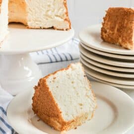 Angel food cake on a white cake platter with large wedges cut on white dessert plates.