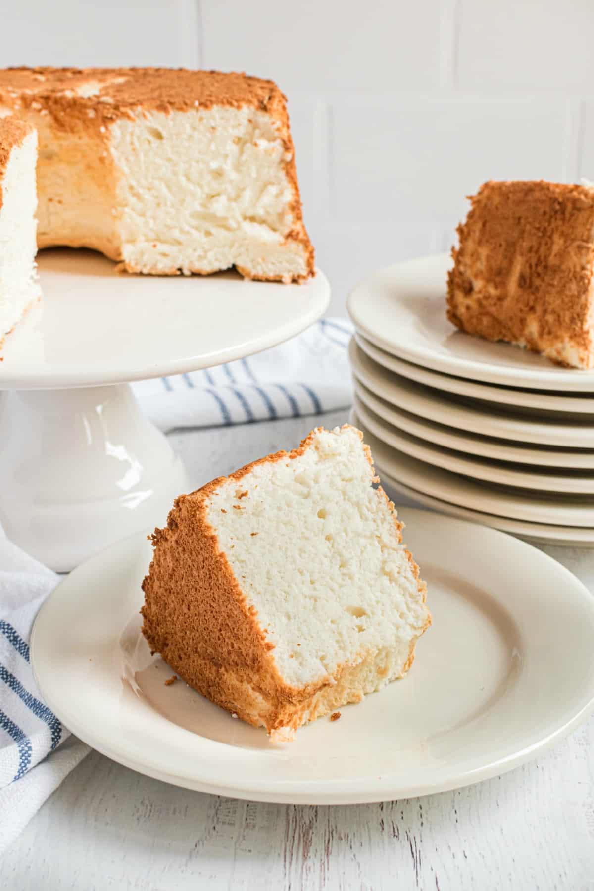 Angel food cake on a white cake platter with large wedges cut on white dessert plates.