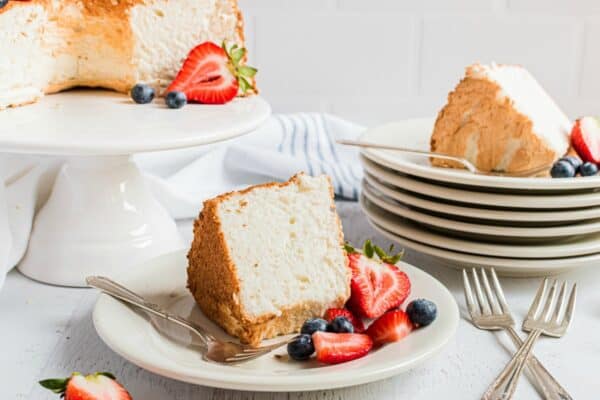 Angel food cake sliced and served on white cake plates with fresh cut berries.