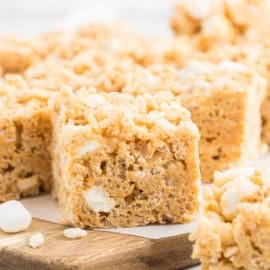 Close-up of Biscoff Rice Krispie Treats with visible marshmallows, cut into squares and placed on a wooden board.
