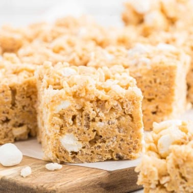 Close-up of Biscoff Rice Krispie Treats with visible marshmallows, cut into squares and placed on a wooden board.