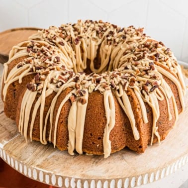 A brown sugar pound cake Bundt topped with caramel glaze and chopped pecans on a wooden cake stand.
