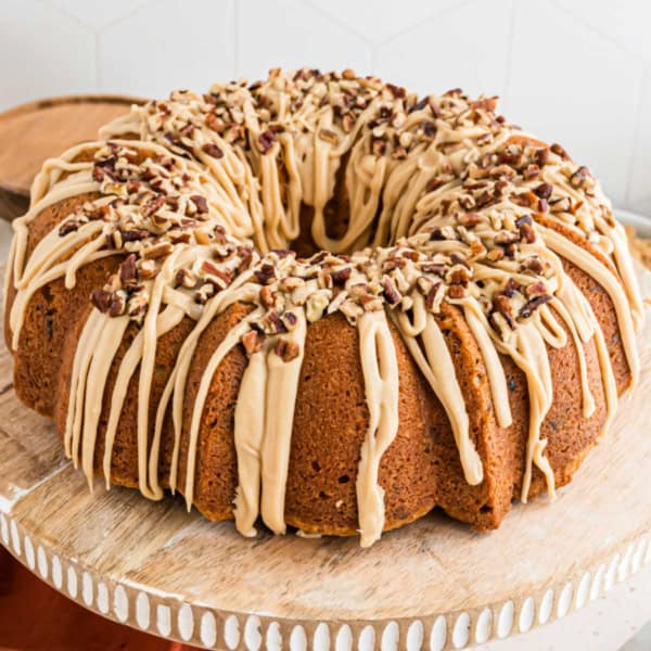 A brown sugar pound cake Bundt topped with caramel glaze and chopped pecans on a wooden cake stand.