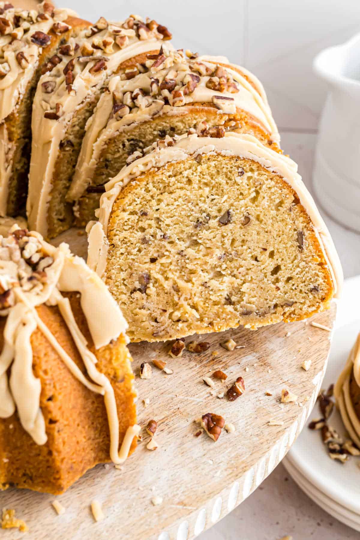 A sliced brown sugar pound cake bundt with icing and chopped pecans on top, displayed on a wooden cake stand.